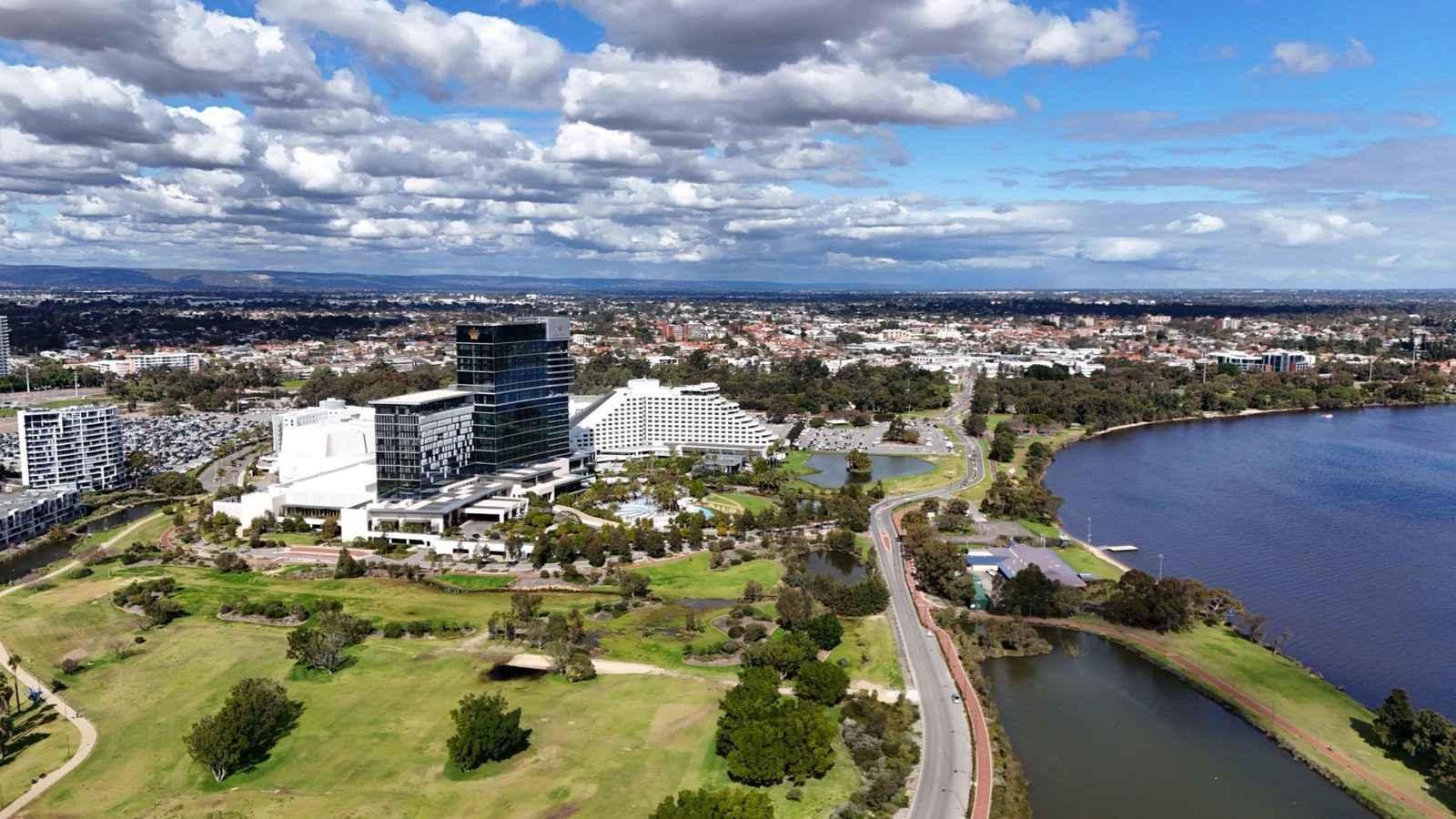 Aerial view over Burswood with parkland, a road and the Swan River, and suburbs stretching to the horizon