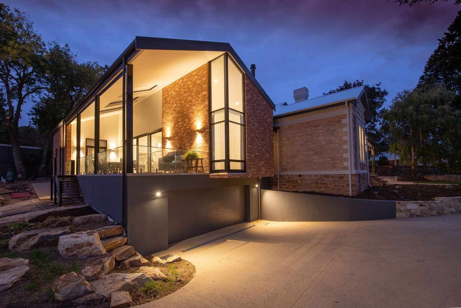 A modern brick home at dusk with a tall gabled wall of floor-to-ceiling windows lit from inside