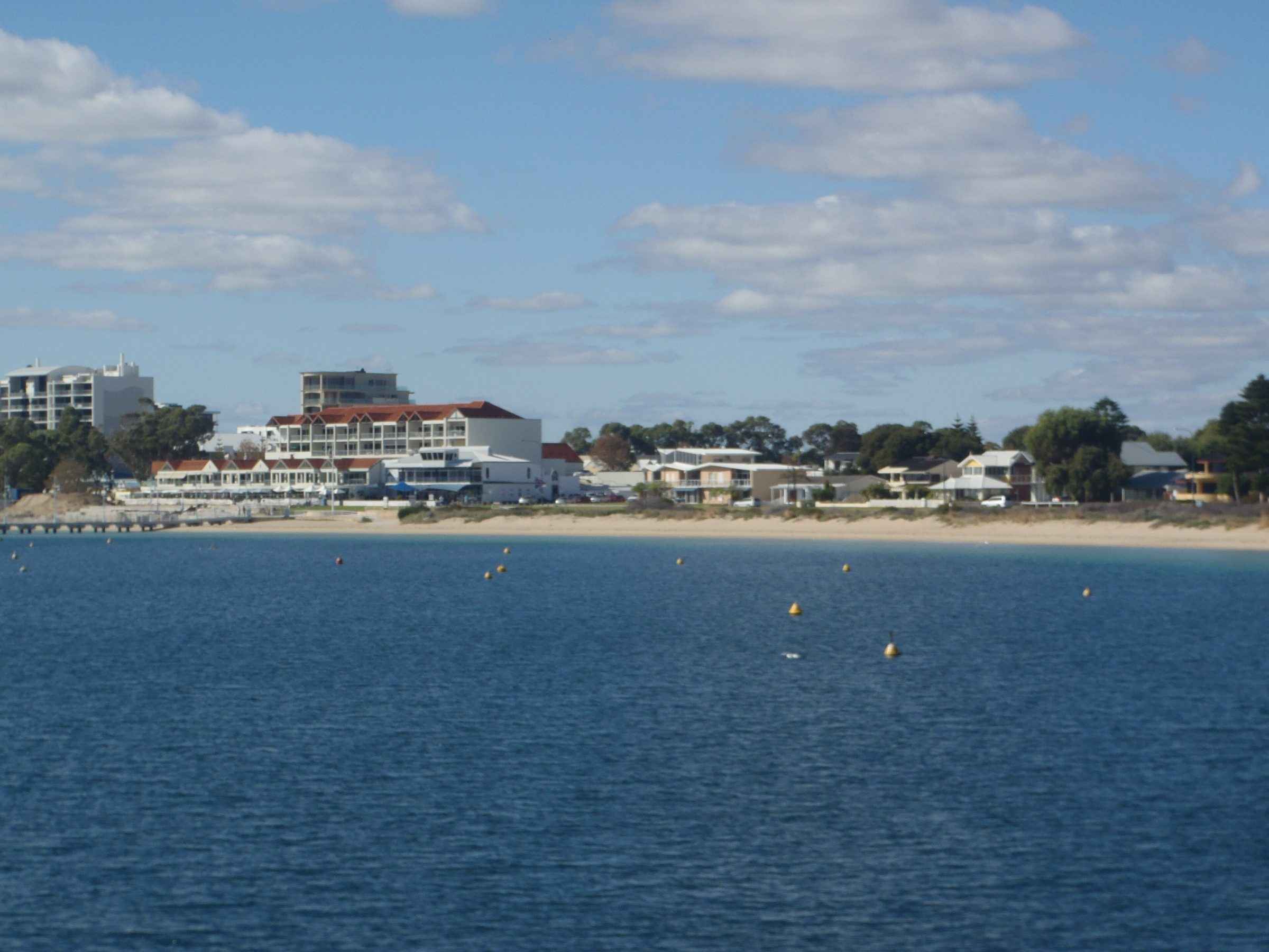 Rockingham seen across the water from Palm Beach Jetty, with low-rise apartments and the beachfront behind moored boats