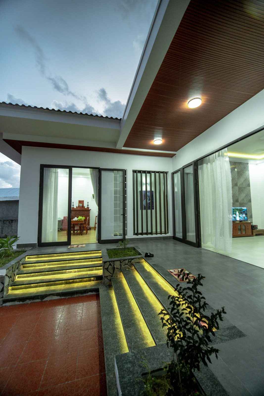 A row of tall glass doors along a covered outdoor area at night, with lit steps and plants in front